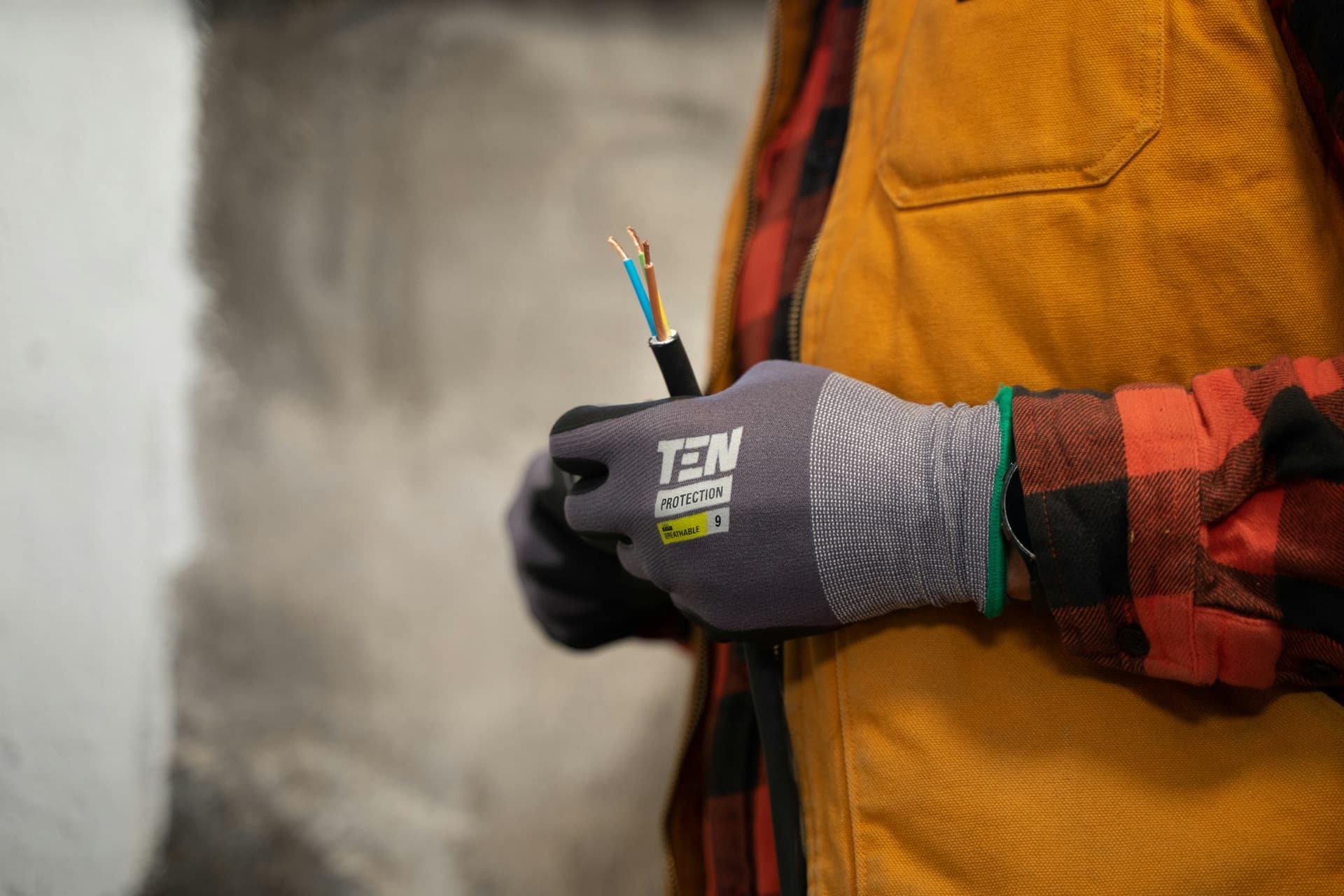 Une main gantée tient un câble dénudé, ses trois fils apparents, sur un chantier